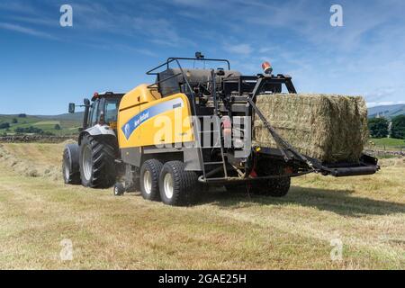 Entrepreneur équipé d'une presse à balles argentée Hurlimann et New Holland, qui fait de grosses balles carrées de foin dans un pré traditionnel des bières, à Hawes, dans le North Yorkshire, au Royaume-Uni. Banque D'Images