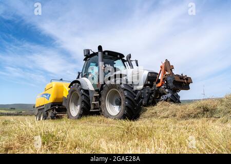 Entrepreneur équipé d'une presse à balles argentée Hurlimann et New Holland, qui fait de grosses balles carrées de foin dans un pré traditionnel des bières, à Hawes, dans le North Yorkshire, au Royaume-Uni. Banque D'Images