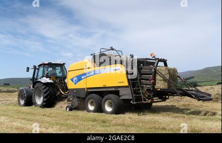 Entrepreneur équipé d'une presse à balles argentée Hurlimann et New Holland, qui fait de grosses balles carrées de foin dans un pré traditionnel des bières, à Hawes, dans le North Yorkshire, au Royaume-Uni. Banque D'Images