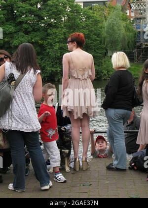 Une grande jeune femme à tête rouge sur le bord de la rivière à Chester, Cheshire, Angleterre. Elle porte une robe courte élégante et des talons hauts. Elle a un chien en tête Banque D'Images