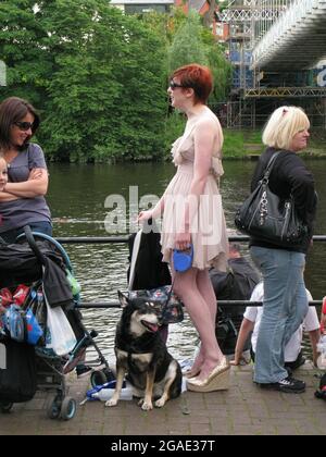 Une grande jeune femme à tête rouge sur le bord de la rivière à Chester, Cheshire, Angleterre. Elle porte une robe courte élégante et des talons hauts. Elle a un chien en tête Banque D'Images