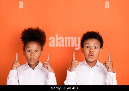 Photo de deux jeunes enfants afro surpris indiquent doigts vide espace décider choisir des annonces isolées sur fond orange couleur Banque D'Images