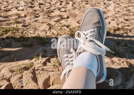 Jambes en baskets grises sur le sable de la plage. Concept de vacances d'été au bord de la mer. Voyage de style de vie. Vue POV. Copier l'espace. Banque D'Images