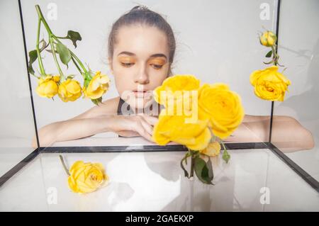 Modèle femelle derrière une boîte en verre avec fleurs Banque D'Images