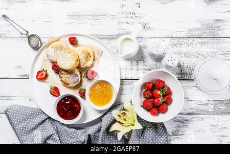 Crêpes au fromage blanc avec fraises fraîches et confiture. Crêpes au fromage cottage sur une assiette blanche arrosée de sucre en poudre. Délicieux break fait maison Banque D'Images