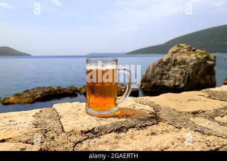 Verre de bière sur fond de mer, gros plan. Une tasse à fogged, un verre de bière froide se dresse contre des paysages flous de mer et de montagne dans le café Banque D'Images