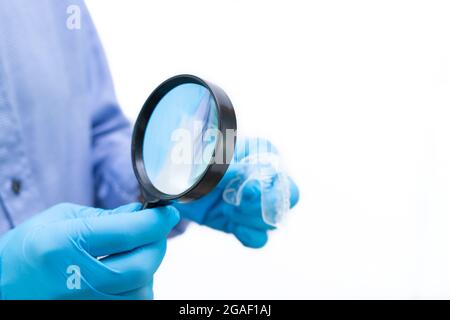 Dentiste en chemise bleue et fond blanc examinant une attelle dentaire avec une loupe. Copier l'espace. Banque D'Images