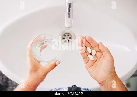 Femme senior prenant des pilules. Les femmes qui boivent des médicaments d'ordonnance, qui tiennent un verre d'eau. Traitement de la drogue. Vue de dessus des mains Banque D'Images