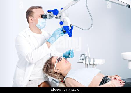 Jolie femme caucasienne en chaise de dentiste dans la clinique dentaire moderne. Le médecin a examiné le patient à l'aide d'un équipement dentaire professionnel, d'un microscope. PA femelle Banque D'Images