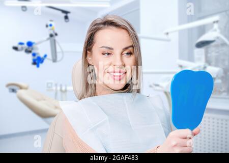 Bonne femme attirante regardant ses dents dans le miroir. Patient satisfait de soins dentaires ou de blanchiment pour le traitement dentaire. Banque D'Images