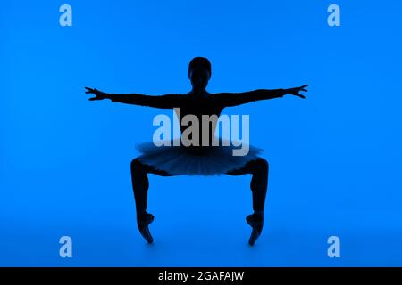 Ballerine non reconnaissable en robe tutu et chaussures pointe faisant le squat debout sur les tiptoes. Femme isolée sur fond bleu. Spectacles de danse de ballet Banque D'Images