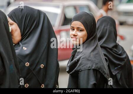 Une jolie jeune fille musulmane portant le hijab debout avec d'autres femmes musulmanes regarde l'épaule en souriant à la caméra, Yangon, Myanmar Banque D'Images