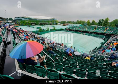 Les spectateurs s'entassent sous des parasols sur la court 12 pendant les championnats de Wimbledon 2021 Banque D'Images