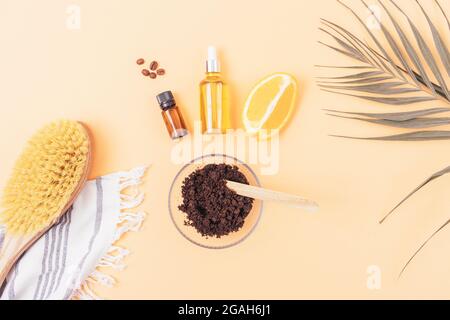 Gommage maison anti-cellulite avec grains de café et huiles naturelles à côté de la brosse de massage, serviette de bain et feuille de palmier, plat. Banque D'Images