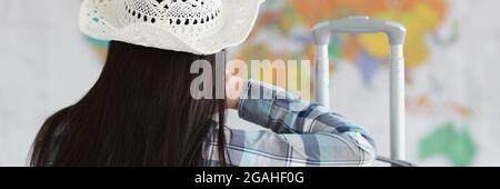 Femme assis avec son dos dans un chapeau blanc et une valise et regarde la carte du monde Banque D'Images