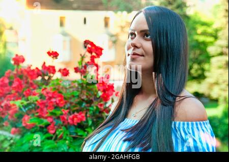 Portrait d'une jeune femme latino-américaine souriante, arrière-plan isolé d'arbres et de fleurs. Émotion humaine positive Banque D'Images