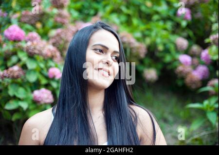 Portrait d'une jeune femme latino-américaine souriante, arrière-plan isolé d'arbres et de fleurs. Émotion humaine positive Banque D'Images