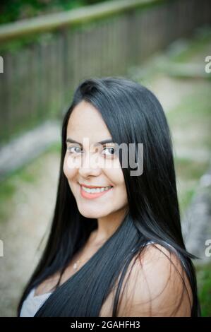 Portrait d'une jeune femme latino-américaine souriante, arrière-plan isolé d'arbres et de fleurs. Émotion humaine positive Banque D'Images