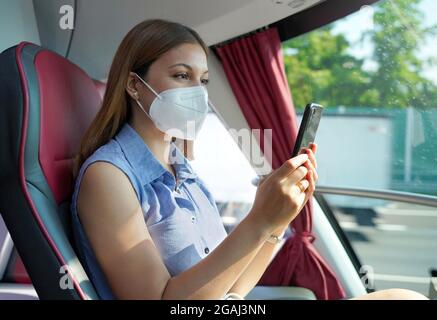 Vue latérale d'une femme détendue avec masque KN95 FFP2 utilisant l'application smartphone. Passager en bus avec masque de protection pour le transport de SMS sur un téléphone portable. Banque D'Images