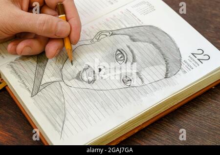 Man dessine un croquis au crayon d'un jeune homme adulte dans un journal ouvert. Portrait noir et blanc d'un homme afro-américain. Sa main gauche tire un petit coup Banque D'Images