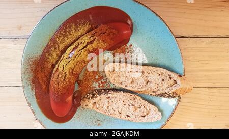 Currywurst allemand traditionnel dans une assiette sur une table en bois dans un café avec du pain. Vue de dessus. Spécialités d'Allemagne et de Berlin. Saucisse épicée Banque D'Images