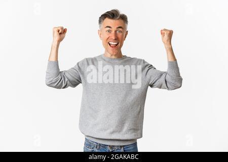 Portrait d'un homme d'âge moyen excité et heureux, célébrant la victoire ou le succès, levant les mains et disant oui, triomphant sur fond blanc Banque D'Images