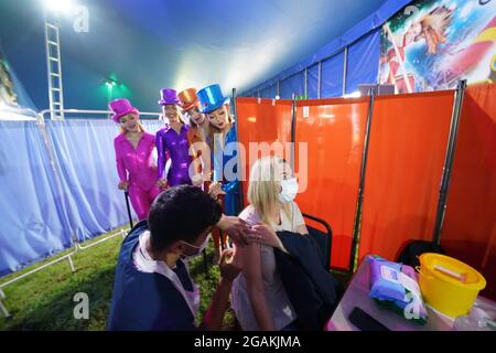 Des artistes de Circus Extreme regardent Rhiannon Alexander, 34 ans, de Bradford, recevoir une vaccination Covid-19 dans une clinique de vaccination pop-up dans le chapiteau du cirque de Halifax. Date de la photo: Samedi 31 juillet 2021. Banque D'Images