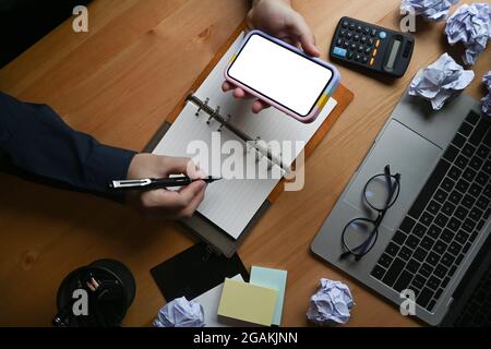 Femme d'affaires tenant un téléphone portable et travaillant au bureau entouré de papier froissé. Banque D'Images