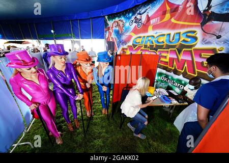 Les artistes de Circus Extreme regardent Rhiannon Alexander, 34 ans, de Bradford, attendre une vaccination Covid-19 dans une clinique de vaccination pop-up dans le chapiteau du cirque de Halifax. Date de la photo: Samedi 31 juillet 2021. Banque D'Images