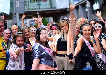 Un groupe de femmes en fête, portant des écouteurs. Sur un 'Silent Adventures' a organisé une discothèque silencieuse et un flash mob, danse avec enthousiasme dans les rues de Manchester, Royaume-Uni, le 31 juillet 2021. Banque D'Images