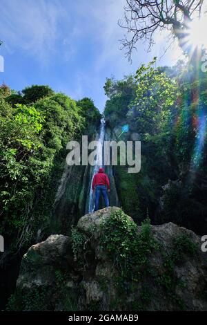 Jeune homme avec une cagoule rouge regardant les cascades de Chorrera de Balastar, Faraján. Coin unique de la province de Malaga en Andalousie Banque D'Images