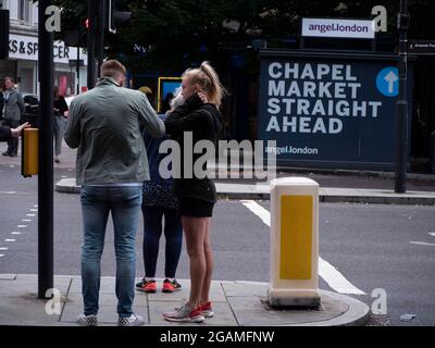 Couple debout sur la route de l'île devant le panneau pour Chapel Street Market à Islington Londres Banque D'Images