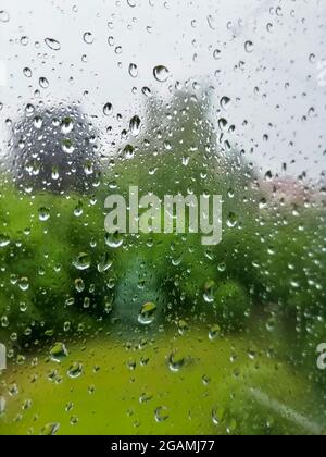 Gouttes de pluie sur une fenêtre par temps pluvieux, fond vert flou Banque D'Images