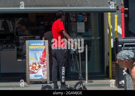 Slough, Berkshire, Royaume-Uni. 20 juillet 2021. Un jeune homme conduit illégalement un e-scooter dans une zone piétonne à la sortie de Slough High Street. Crédit : Maureen McLean/Alay Banque D'Images