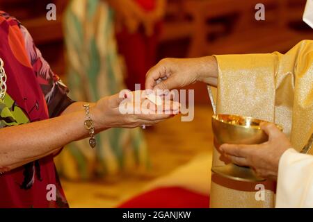 Rite de communion pendant la messe dans une église catholique. Le prêtre donne l'hôte entre les mains d'un fidèle Banque D'Images