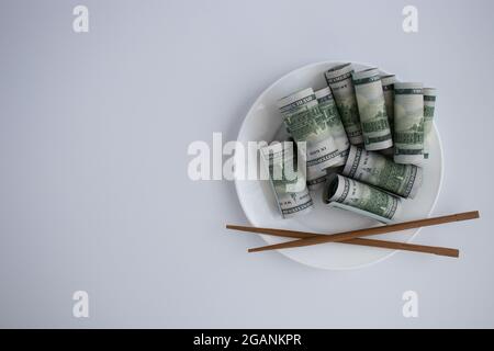 Dollars dans une plaque avec des baguettes de bois sur un fond blanc. Banque D'Images