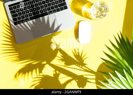 Espace de travail de bureau d'été tendance. Ordinateur portable avec ombre au soleil sur fond jaune Banque D'Images