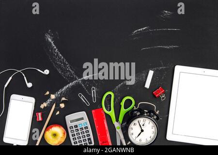 Fournitures de bureau et gadgets numériques sur fond noir de tableau noir. Retour à l'école Banque D'Images