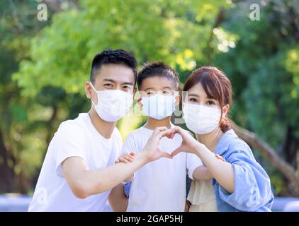 Famille heureuse portant des masques médicaux de protection contre le covid-19 et montrant le mouvement de coeur de main Banque D'Images