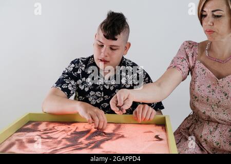 Les enfants ayant un handicap se font une activité sensorielle plateau de sable, table de sable pour l'animation, infirmité motrice cérébrale jouant au jeu apaisant, entraînement moteur fin Banque D'Images