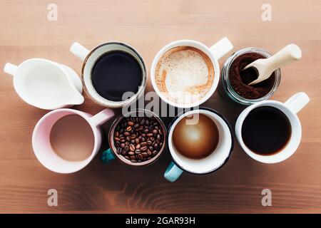 Plusieurs tasses à café et tasses multicolores avec americano, espresso, latte et cappuccino, pot à lait, grains de café rôtis en bouteille de verre, cuillère en bois Banque D'Images