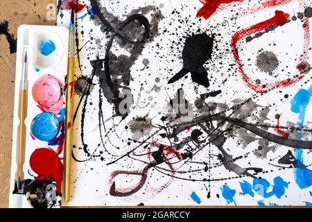 Un gros plan d'une peinture couleur d'aquarelle désordonnée, sur papier blanc avec des outils Banque D'Images