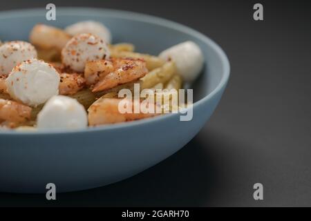 Pâtes Penne aux crevettes et mozzarella et pesto dans un bol bleu avec espace de copie, peu profond Banque D'Images