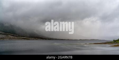 Vue panoramique sur un fjord avec brouillard mystique et couverture nuageuse descendant des montagnes au-dessus de l'océan Banque D'Images