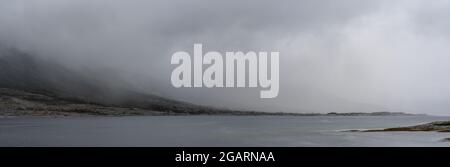 Vue panoramique sur un fjord avec brouillard mystique et couverture nuageuse descendant des montagnes au-dessus de l'océan Banque D'Images