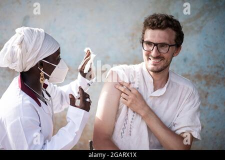 DANS cette image, une infirmière noire portant un masque de protection, avec une seringue et un manomètre dans ses mains, se prépare à injecter une dose de rappel de vaccin dans le ar Banque D'Images