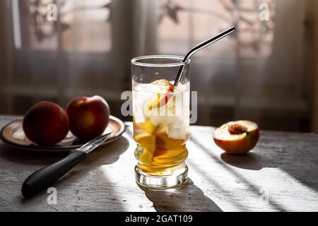 Boisson rafraîchissante d'été avec pêches fraîches sur une table en bois blanc ancienne au soleil près de la fenêtre Banque D'Images