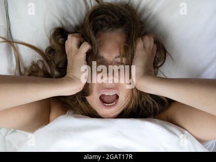 Jeune femme malheureuse dépressive couchée au lit avec des problèmes de santé, hurlant, gueule de bois, dépression, femme sans sommeil, migraine vue du dessus avec des draps blancs Banque D'Images