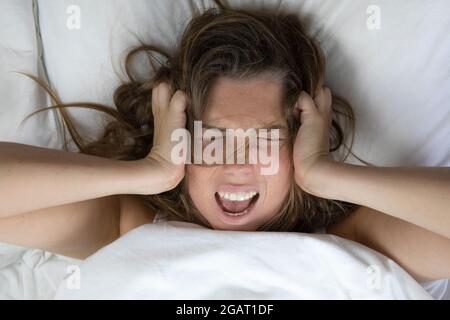 Jeune femme malheureuse dépressive couchée au lit avec des problèmes de santé, hurlant, gueule de bois, dépression, femme sans sommeil, migraine vue du dessus avec des draps blancs Banque D'Images