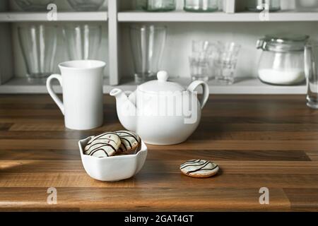 Petits gâteaux dans un bol blanc, théière et tasse de thé sur la table en bois, concept matin et petit déjeuner Banque D'Images